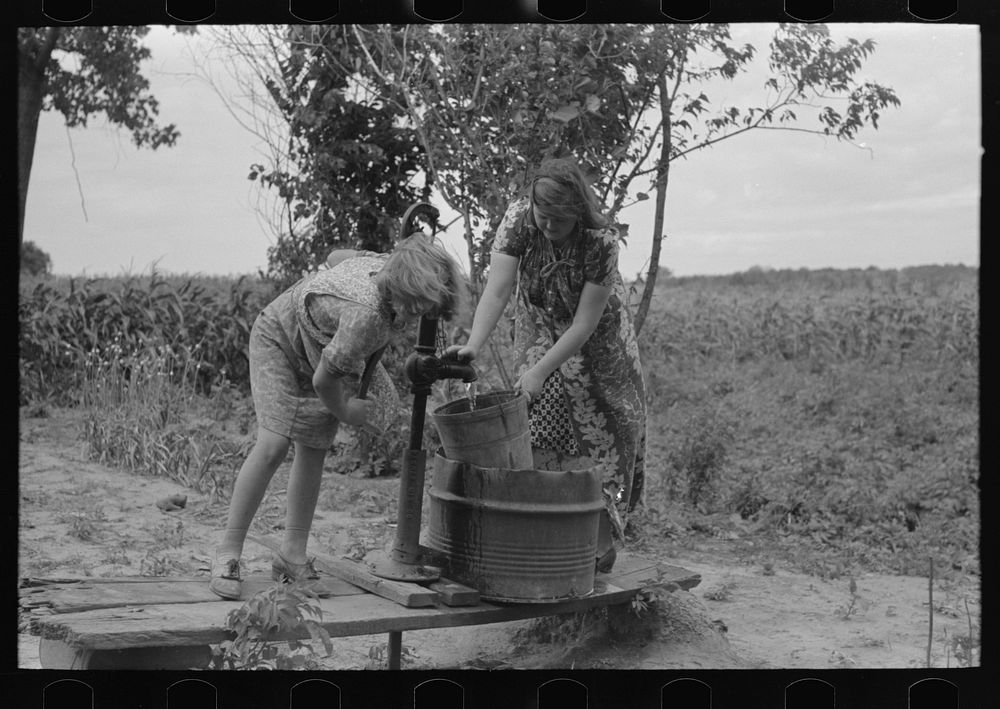 Pumping water near Muskogee, Oklahoma. Daughters of farmer about to migrate to California by Russell Lee