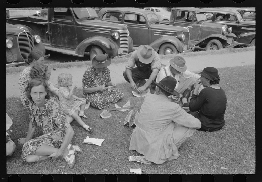 Farm people eating watermelon on lawn in front of courthouse, Tahlequah, Oklahoma by Russell Lee