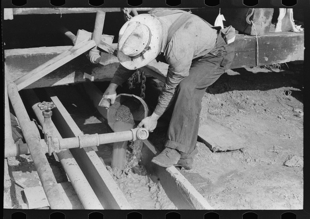 Oil field worker examining mud to determine characteristics of stratum through which drilling is being done, Seminole oil…