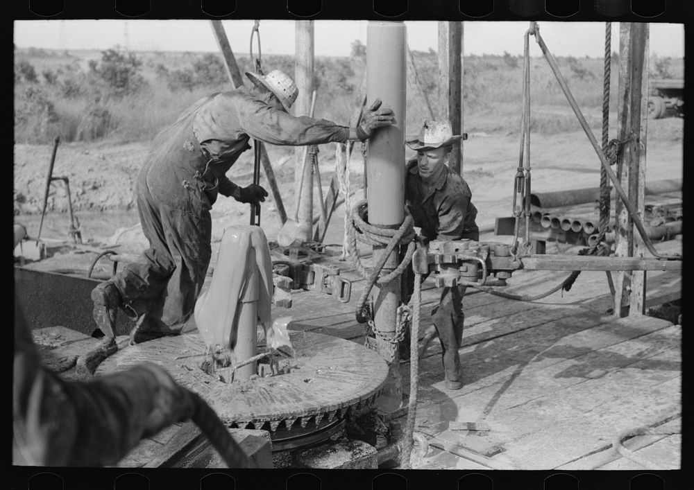 Adding a length of drilling pipe at oil well in the Seminole oil field, Oklahoma. Clamps are put in place; wrench applied to…