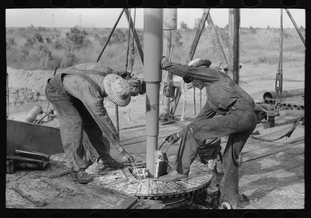 Adding a length of drilling pipe at oil well in Seminole oil field, Oklahoma. Clamps are put in place by Russell Lee