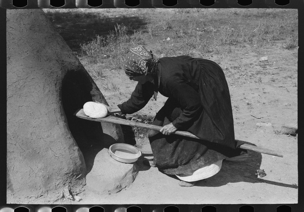 Spanish-American woman putting loaf of bread into oven, Taos County, New Mexico by Russell Lee