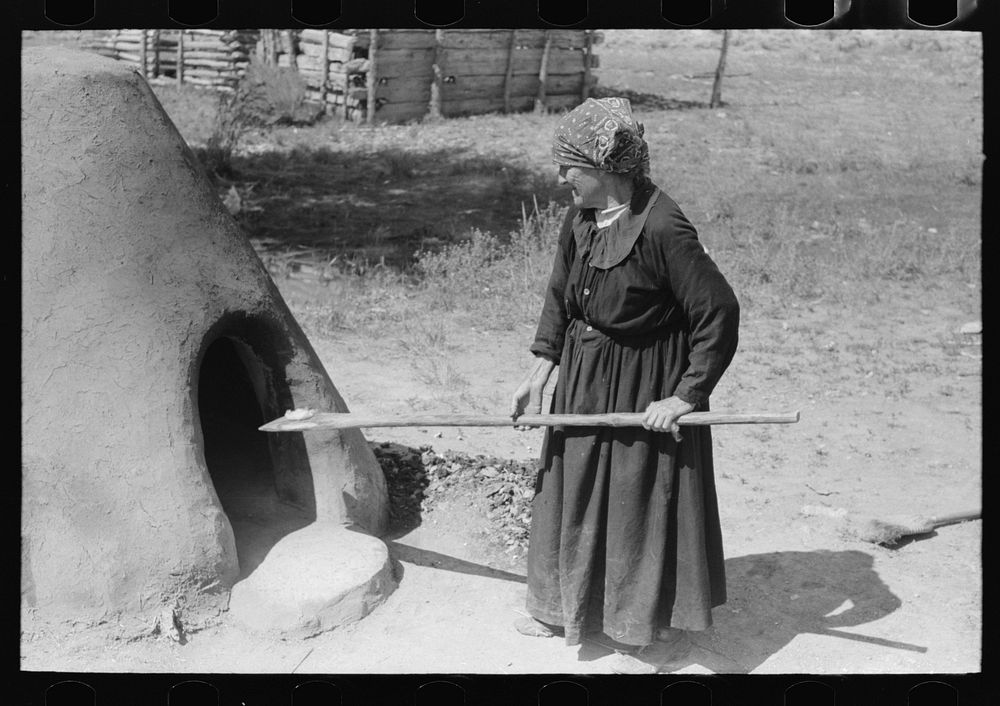 Spanish-American woman testing temperature of earthen oven by determining length of time required to scorch wool, Taos…