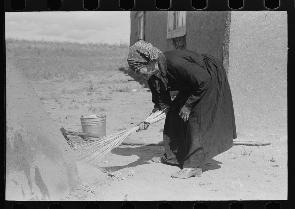 Sweeping hot coals from outdoor earthen oven after it has been heated to proper temperature to bake bread, Taos County, New…