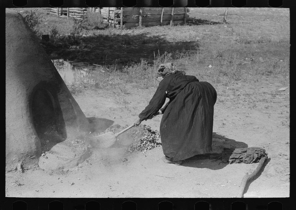 Sweeping coals and ashes from oven before baking bread, Taos County, New Mexico by Russell Lee