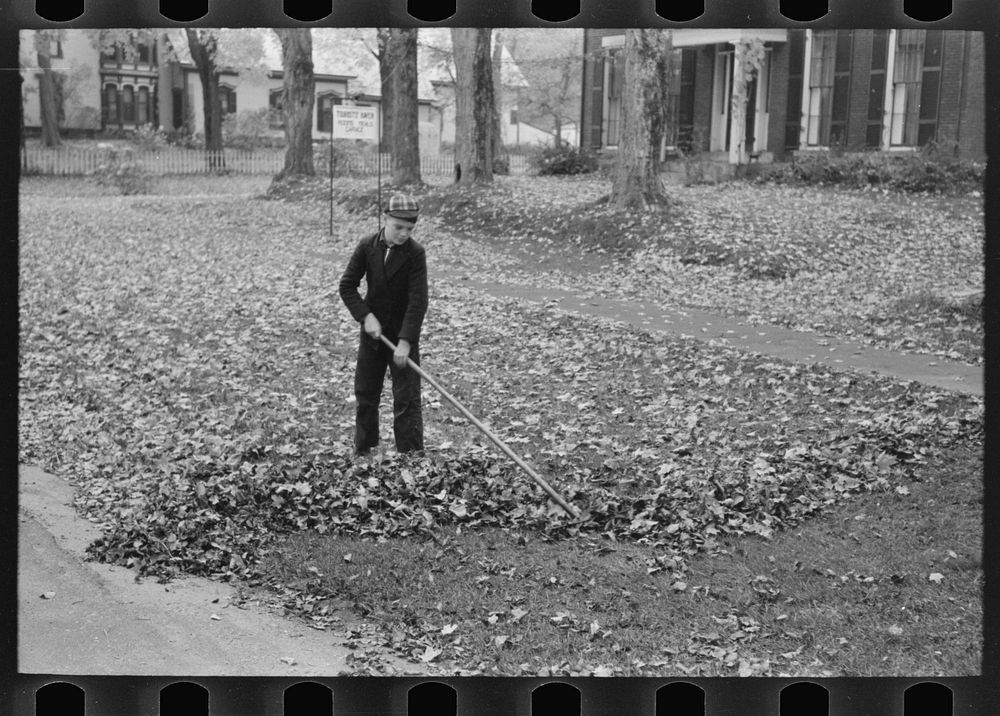 Boy raking and gathering leaves on front lawn, Bradford, Vermont by Russell Lee