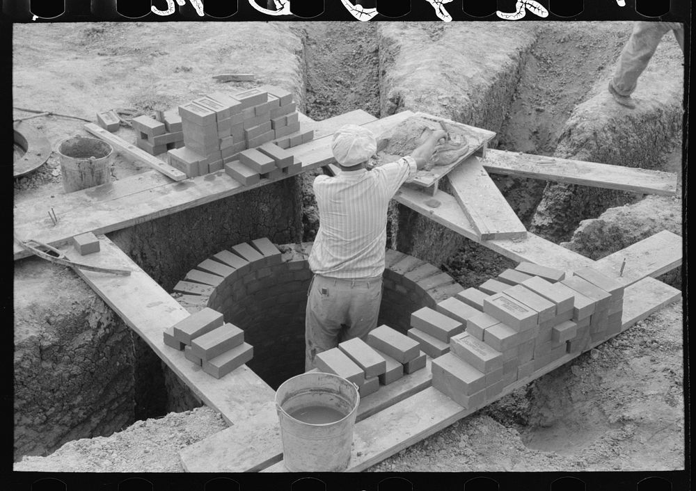 Laying bricks in construction of manhole at migrant camp at Sinton, Texas by Russell Lee