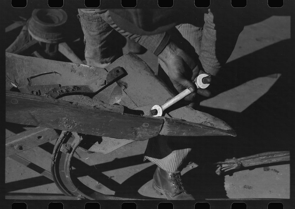 Blacksmith's helper disassembling plow belonging to Pomp Hall,  tenant farmer from Creek County, Oklahoma. Blacksmith shop…