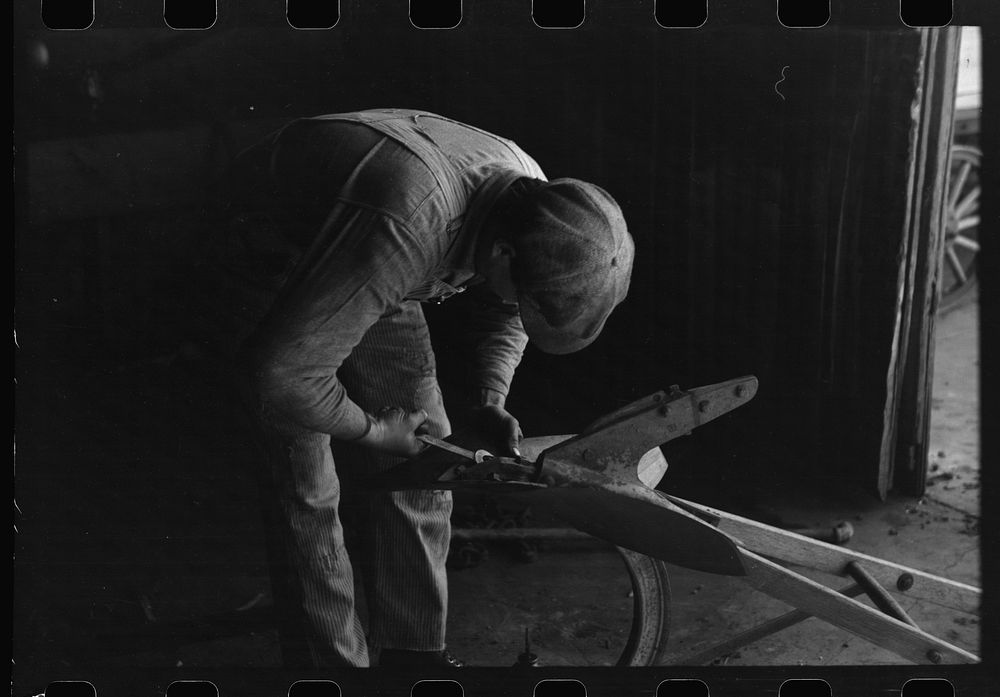[Untitled photo, possibly related to: Blacksmith's helper disassembling plow belonging to Pomp Hall, tenant farmer from…