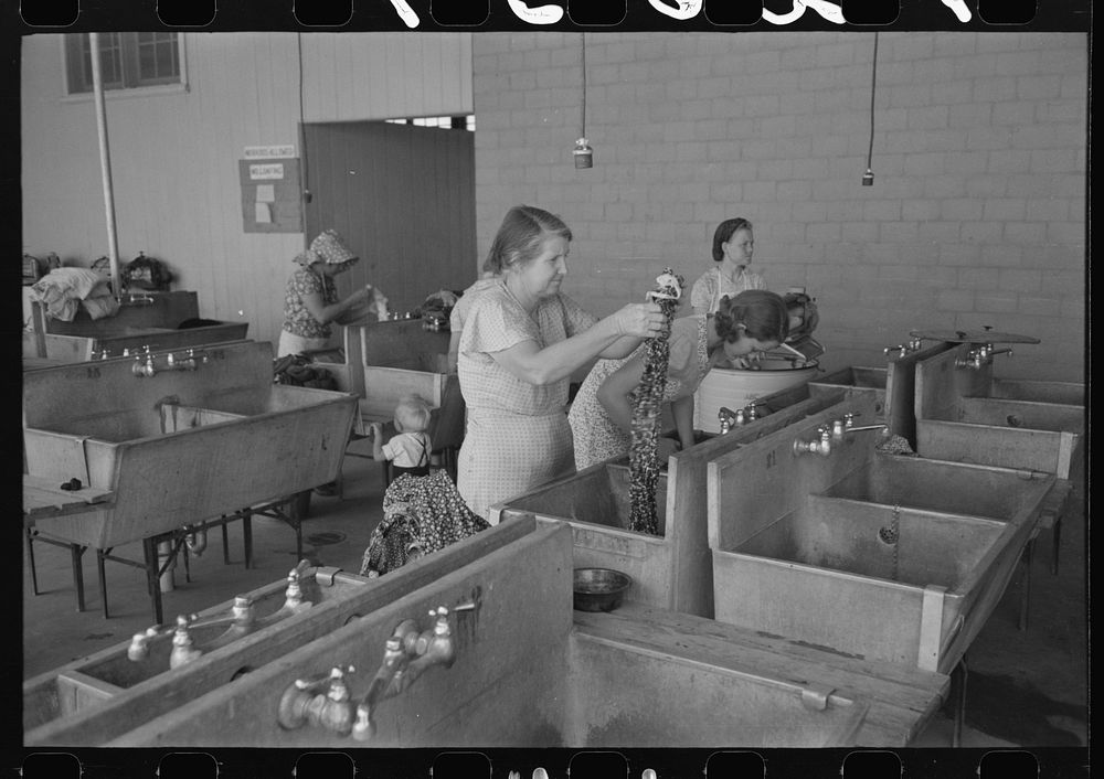 Wives of migratory workers in the laundry room at the Agua Fria Migratory Labor Camp, Arizona. Hot and cold water are…