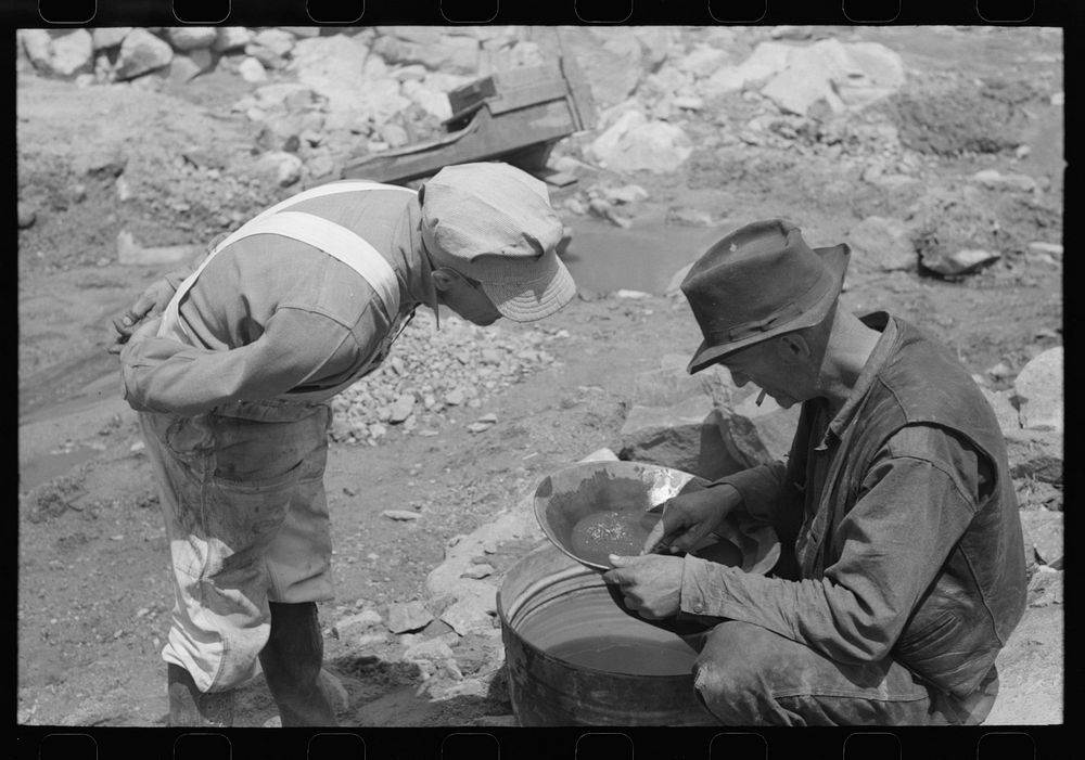 Miner on right examining a "pan" while the visiting prospector watches. Pinos Altos, New Mexico by Russell Lee