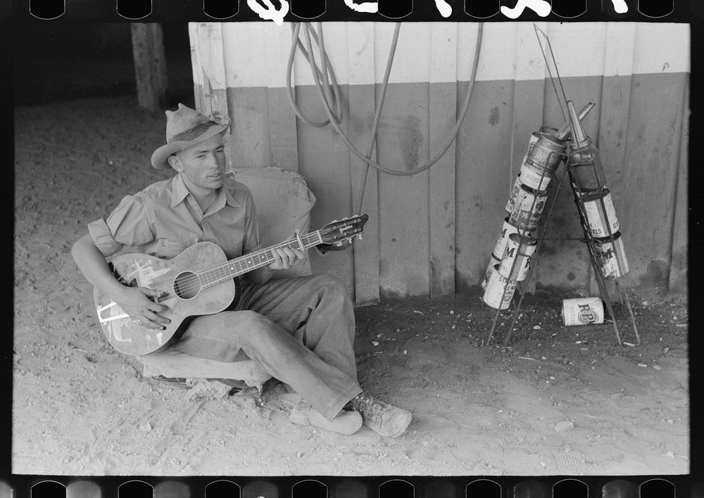 [Untitled photo, possibly related to: Farm boy playing guitar in front of the filling station and garage, Pie Town, New…