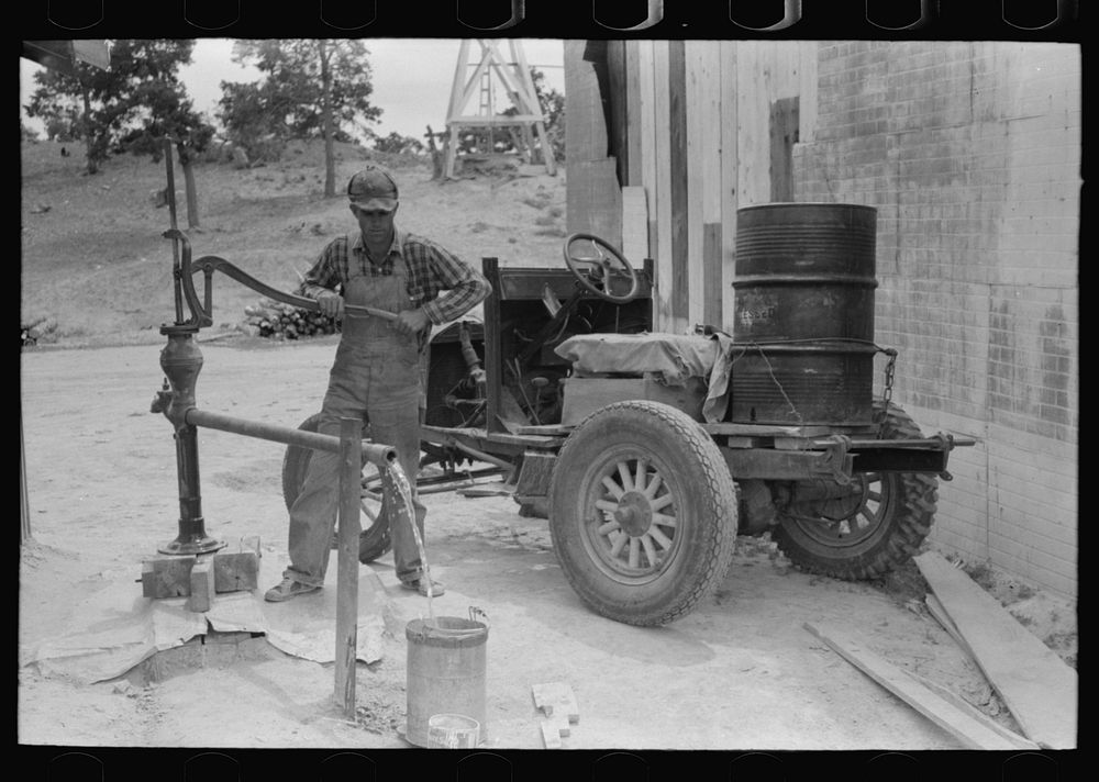 [Untitled photo, possibly related to: Homesteader pumping water which he will haul home from town. Wells require cash to…
