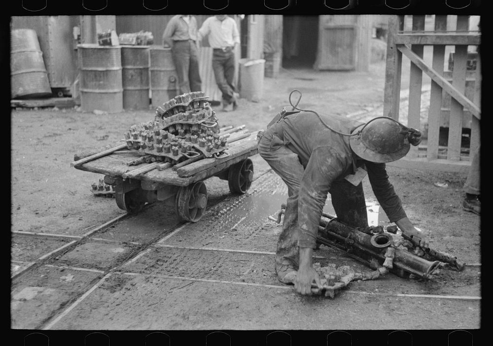 Miner picking up drilling equipment to put on truck, Mogollon, New Mexico by Russell Lee