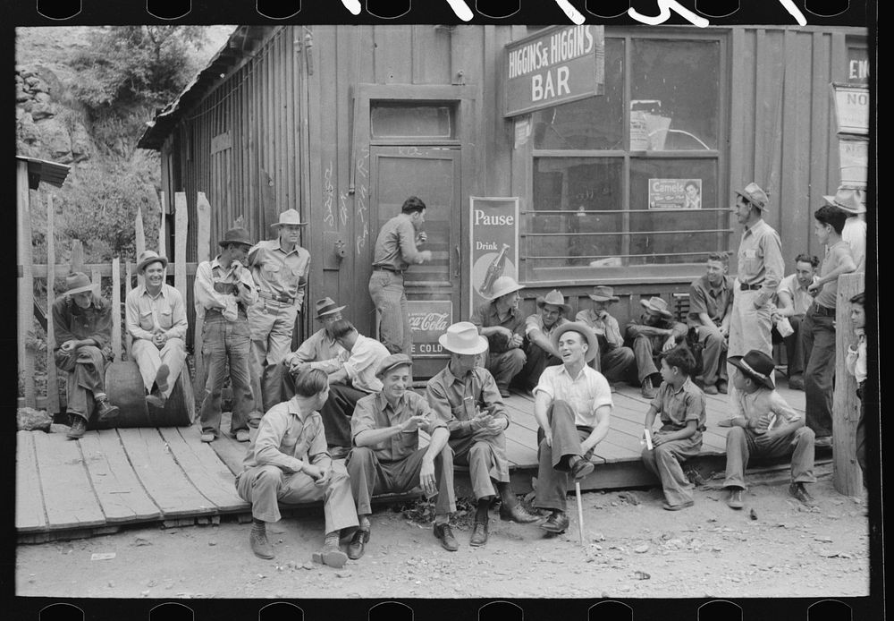 [Untitled photo, possibly related to: Crowd of men sitting on board walk in front of bar at Mogollon, New Mexico, gold…