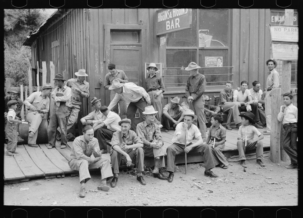 Crowd of men sitting on board walk in front of bar at Mogollon, New Mexico, gold mining town by Russell Lee