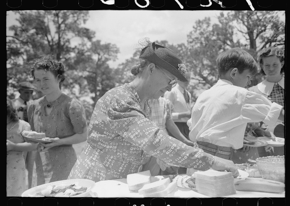 Farm woman arranging food on table at dinner during all day community sing, Pie Town, New Mexico by Russell Lee