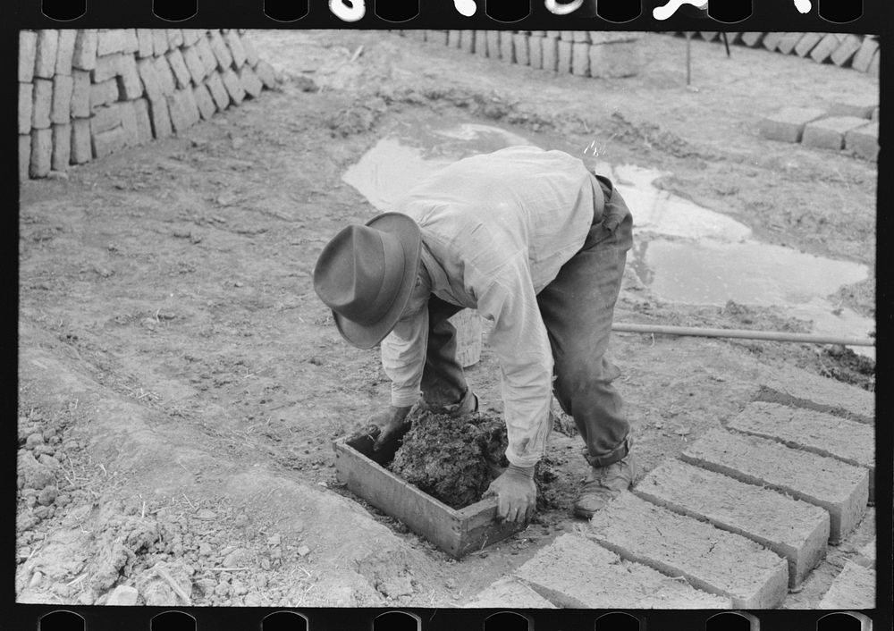 Wooden form is placed over adobe mixture in making bricks, Chamisal, New Mexico by Russell Lee