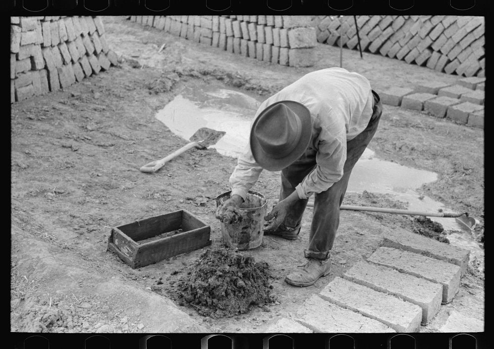 Adding water to adobe mixture for making bricks, Chamisal, New Mexico by Russell Lee