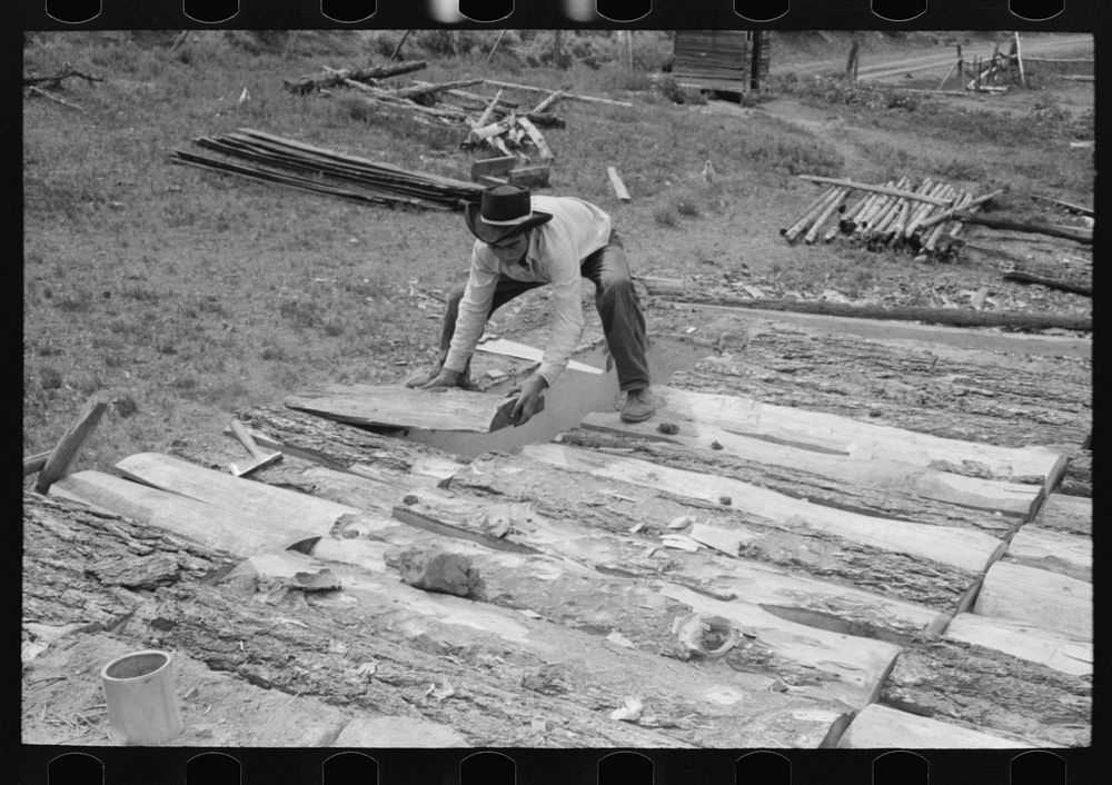 Spanish-American boy building a new roof for his home. Slabs of wood are used as a support for the mud that is later spread…