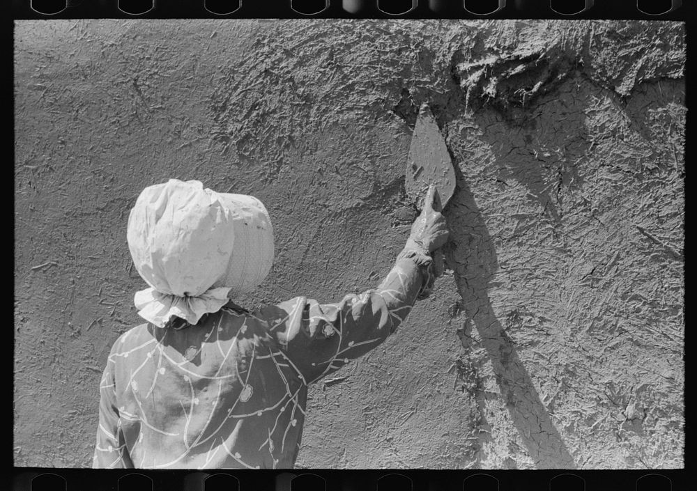 Spanish-American woman plastering adobe house, Chamisal, New Mexico by Russell Lee