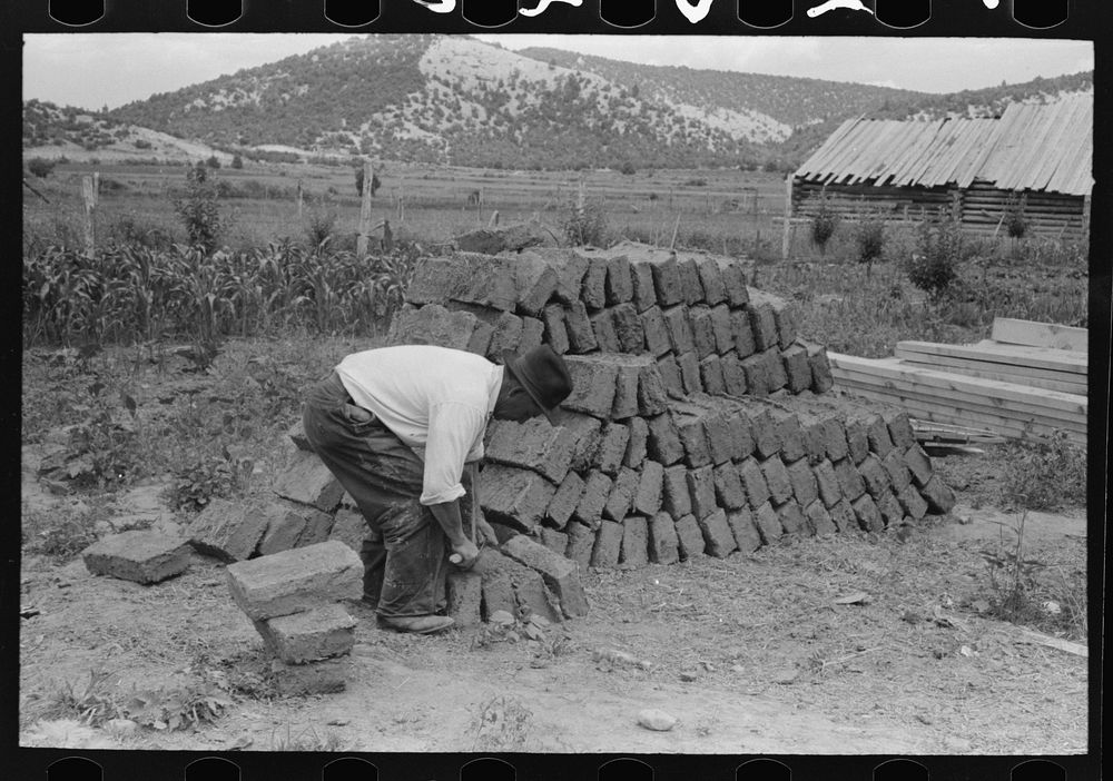 Adobe bricks, shaving one down to size, Penasco, New Mexico by Russell Lee