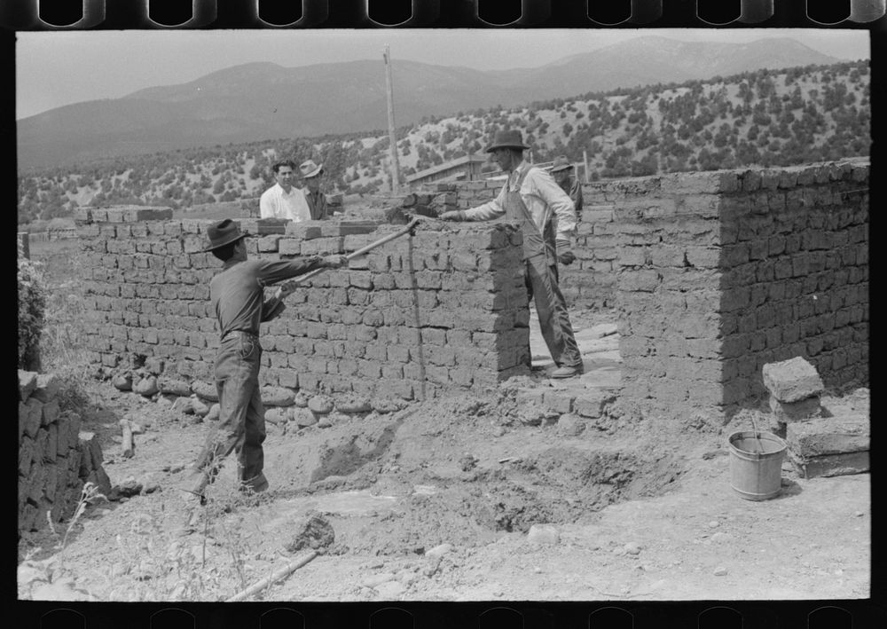 Plaster for adobe bricks to be used in building house is made from dirt dug in the front yard, Penasco, New Mexico by…