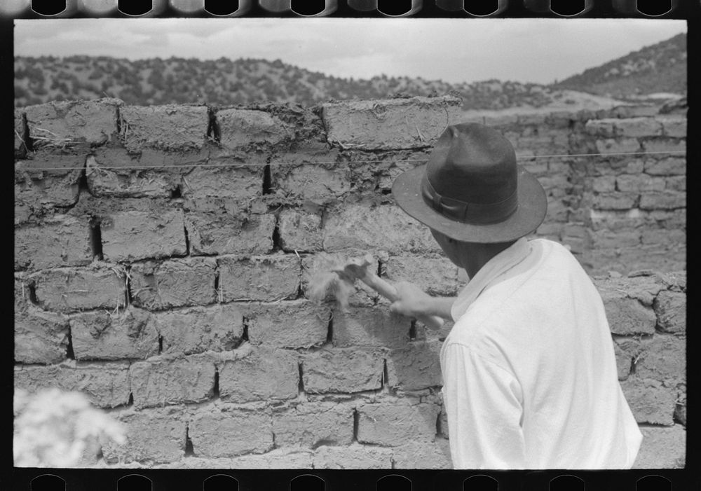 Shaping up wall made of adobe bricks to remove rough or uneven edges, Penasco, New Mexico by Russell Lee