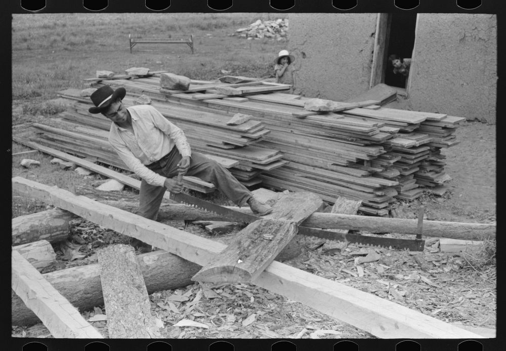 Son of Spanish-American farmer sawing slabs of wood to size for use in roof construction, Amalia, New Mexico by Russell Lee