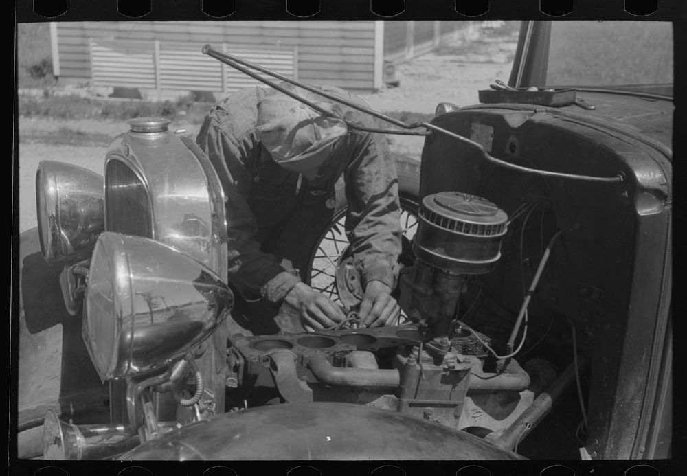 [Untitled photo, possibly related to: Farm worker at work on his automobile. FSA (Farm Security Administration) labor camp.…