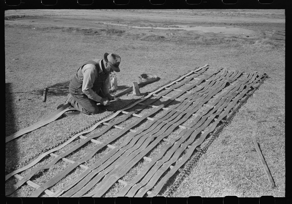Farmer repairs conveyor belt which is used on a hay baler. Imperial County, California by Russell Lee