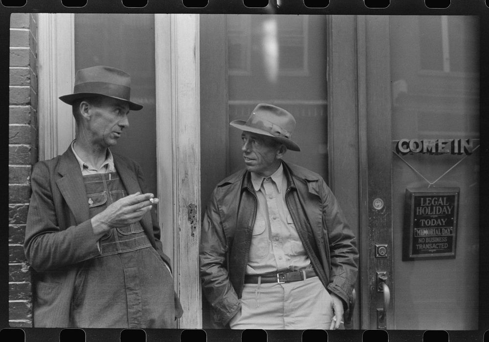Two farmers talking outside of a main street bank, Roxboro, North Carolina, Memorial Day. Sourced from the Library of…