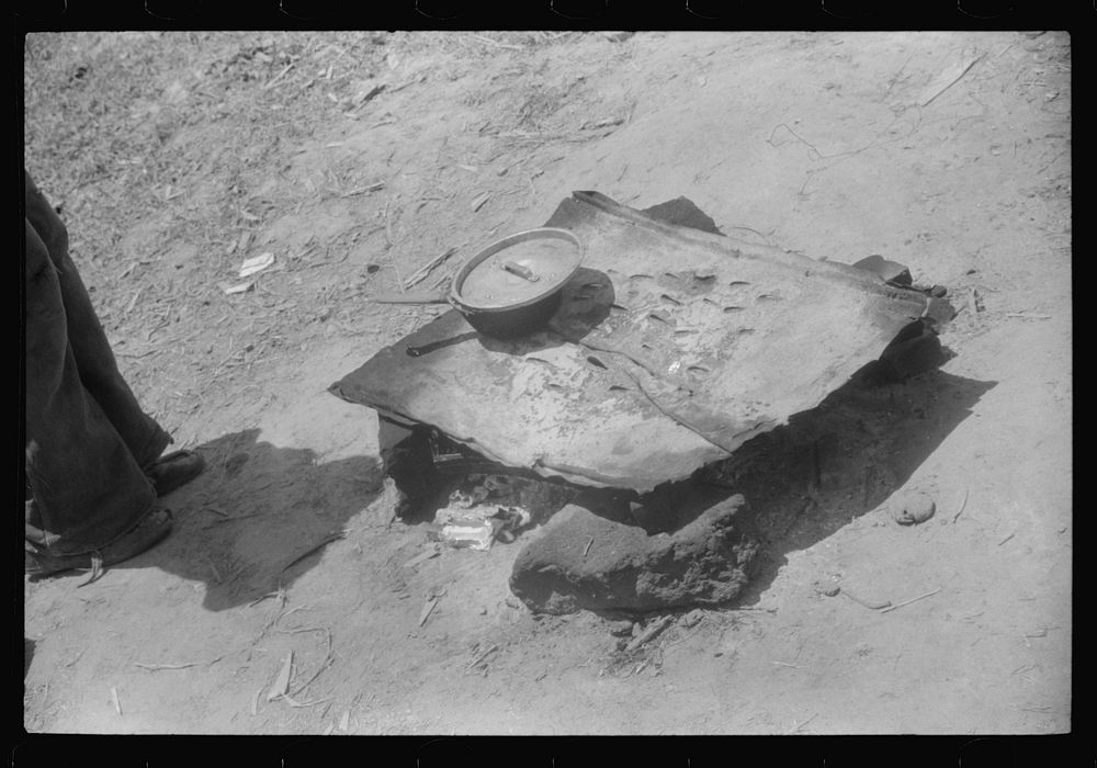 [Untitled photo, possibly related to: Migratory worker getting a light from the improvised stove over which he had cooked…