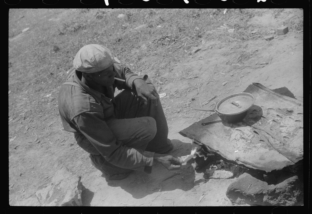 Migratory worker getting a light from the improvised stove over which he had cooked his lunch. Camden, North Carolina.…