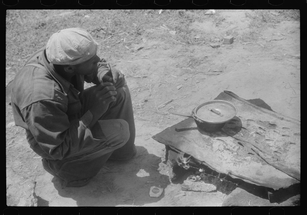 [Untitled photo, possibly related to: Migratory worker getting a light from the improvised stove over which he had cooked…