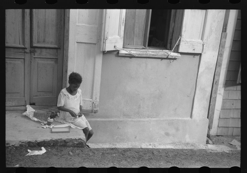 Little girl playing with her Christmas presents on a side street in Charlotte Amalie, Virgin Islands. Sourced from the…