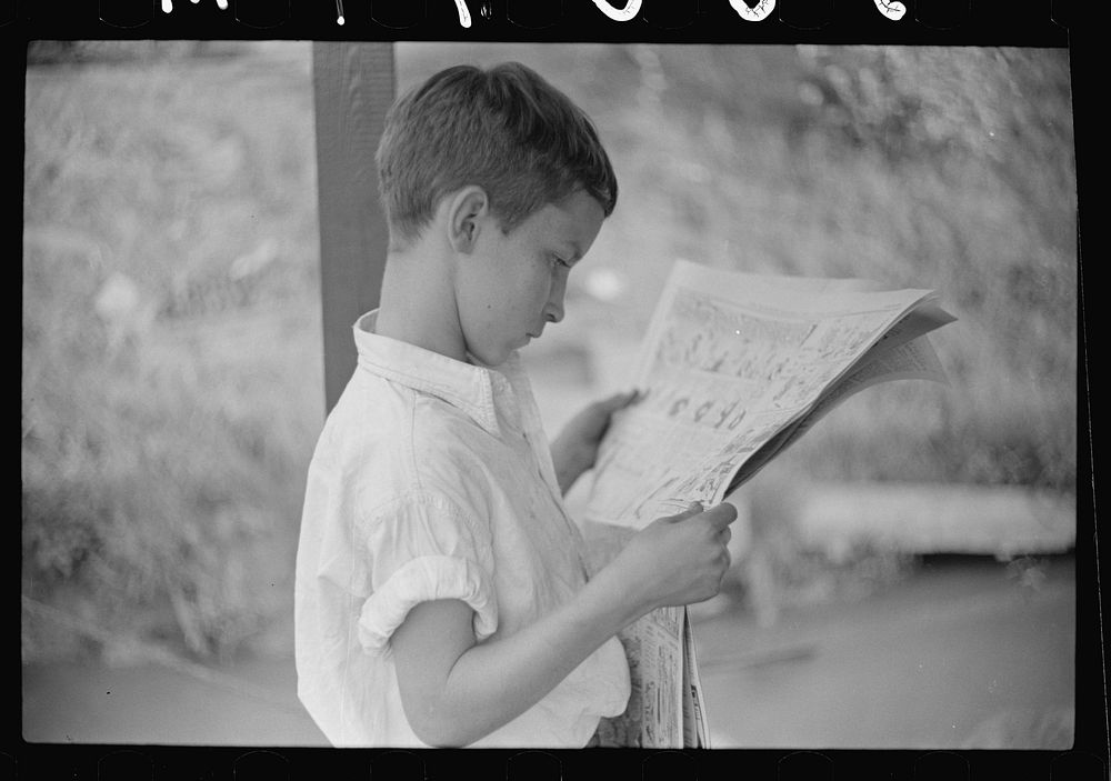 Son of man living on houseboat on river reading paper. Charleston, West Virginia. Sourced from the Library of Congress.