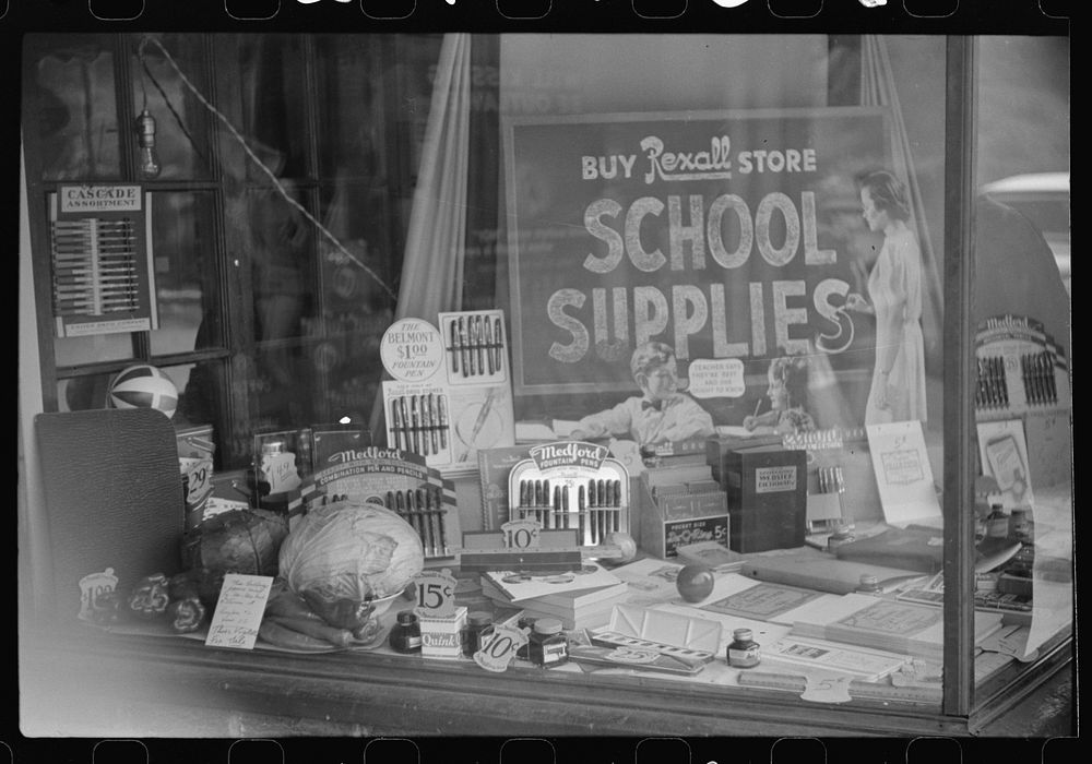 Vegetables (at left) and school supplies in drug store window in mining town. Osage, West Virginia. Sourced from the Library…