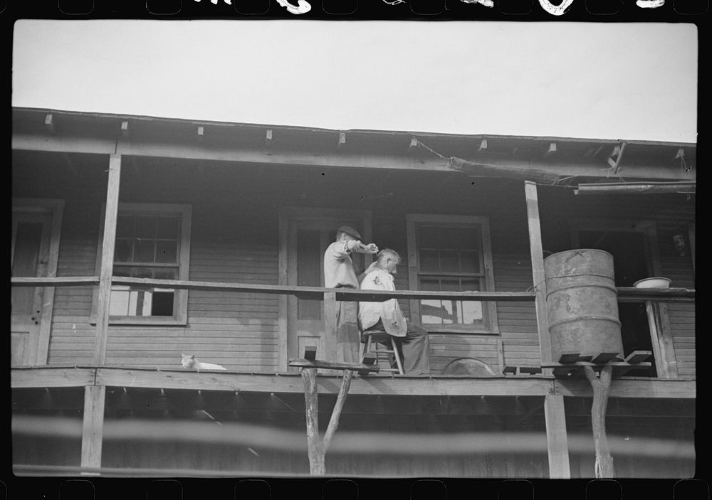 Miners very often give each other haircuts on front porch. Note rain barrel. The "Patch," Chaplin, West Virginia. Sourced…