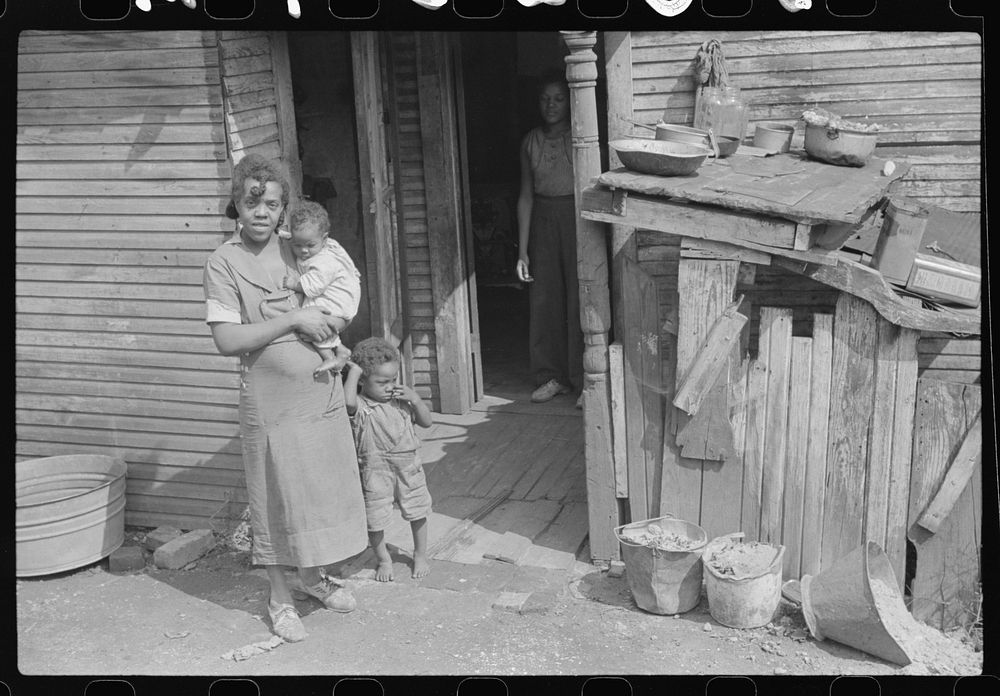 Coal miner's wife and children (note child's legs) in back of their home. Bertha Hill, West Virginia. Sourced from the…