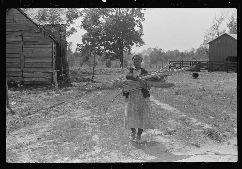 Aunt Nellie Pettway, carrying wood from yard for fireplace. Gees Bend, Alabama. Sourced from the Library of Congress.