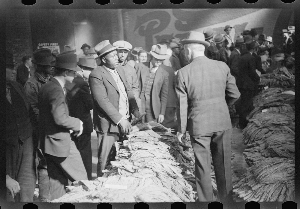  farmer talking with warehouse man about price he received at auction for his tobacco, Durham, North Carolina. Sourced from…