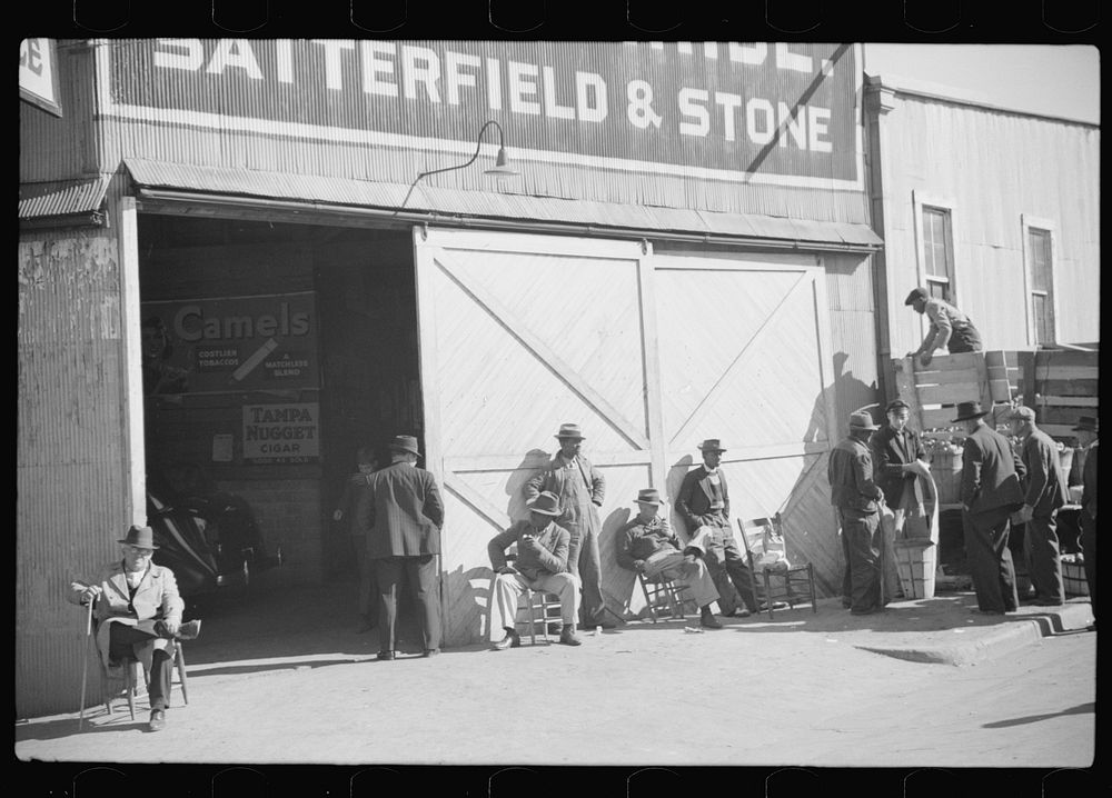 Farmers waiting and buying apples outside warehouse during tobacco auctions. Durham, North Carolina. Sourced from the…
