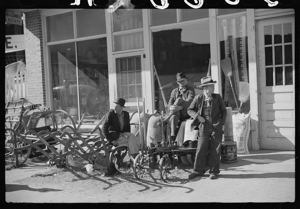 [Untitled photo, possibly related to: Farmers waiting around in front of farmer's supply company next to tobacco warehouse…