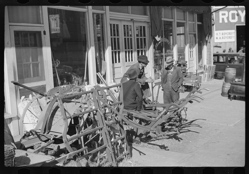 [Untitled photo, possibly related to: Farmers waiting around in front of farmer's supply company next to tobacco warehouse…