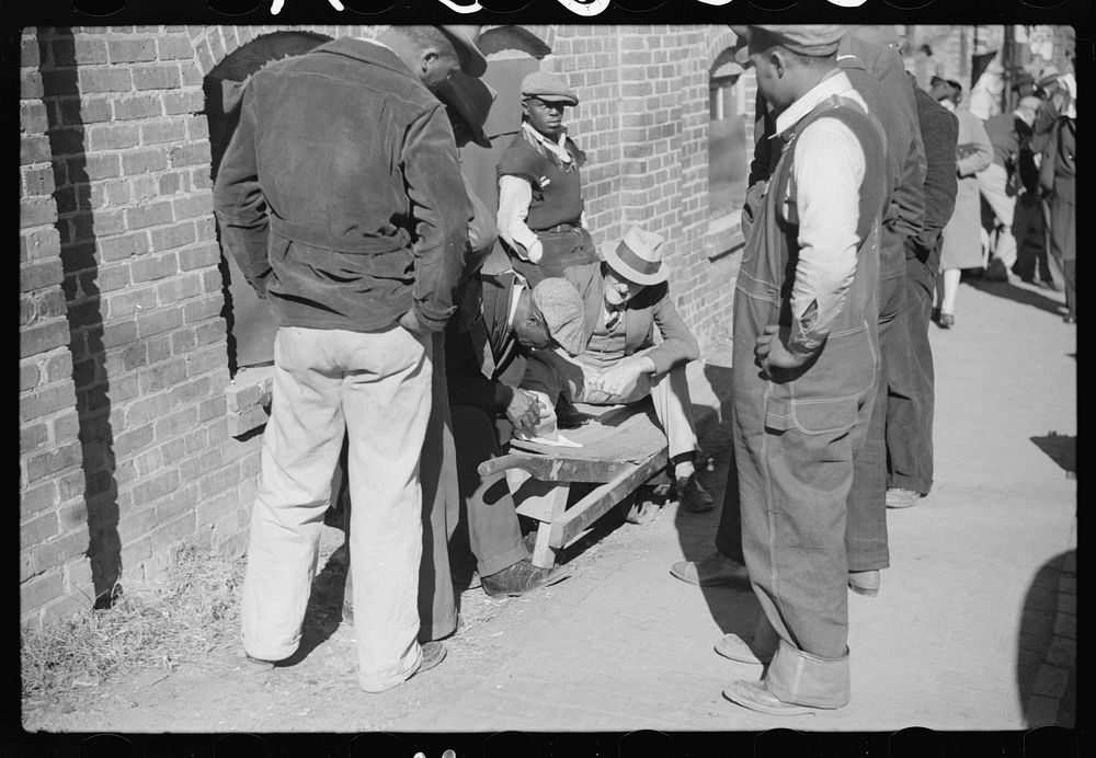 Farmer having corn removed from his foot on street outside tobacco warehouse during auction sales, Durham, North Carolina.…