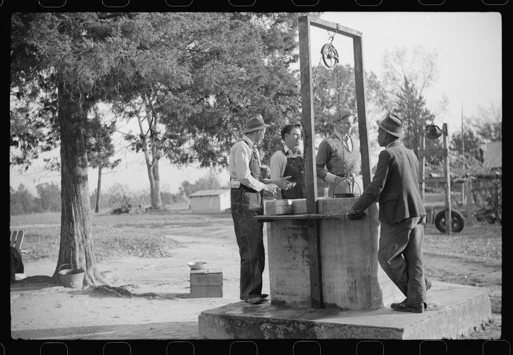 [Untitled photo, possibly related to: Men drinking from well on farm near the Fred Wilkins place. They have been shucking…