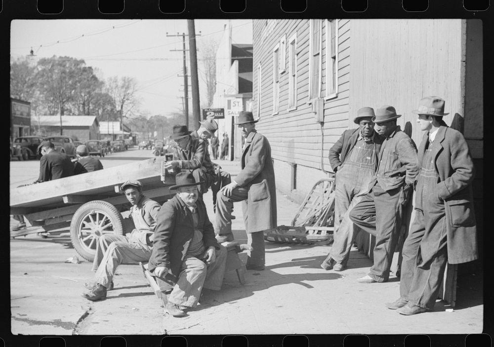 Farmers waiting around outside warehouse for tobacco auction sale to begin. Tobacco was brought in trailer to warehouse.…