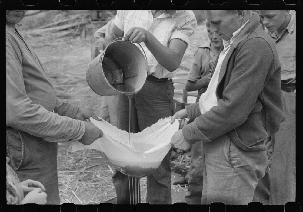 Pouring off and straining finished sorghum syrup after it had been boiled down at a "syruping off" on the highway between…