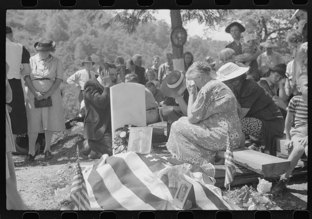 Mother and relatives weeping at the grave of deceased at memorial meeting. Preacher, with hands over ears, is praying. Near…